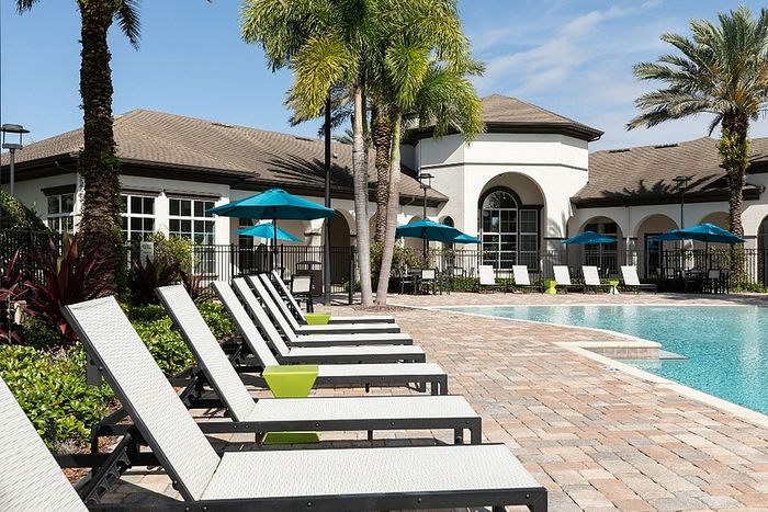 Luxurious poolside view at modern apartment complex featuring elegant lounge chairs, vibrant umbrellas, and lush palm trees.