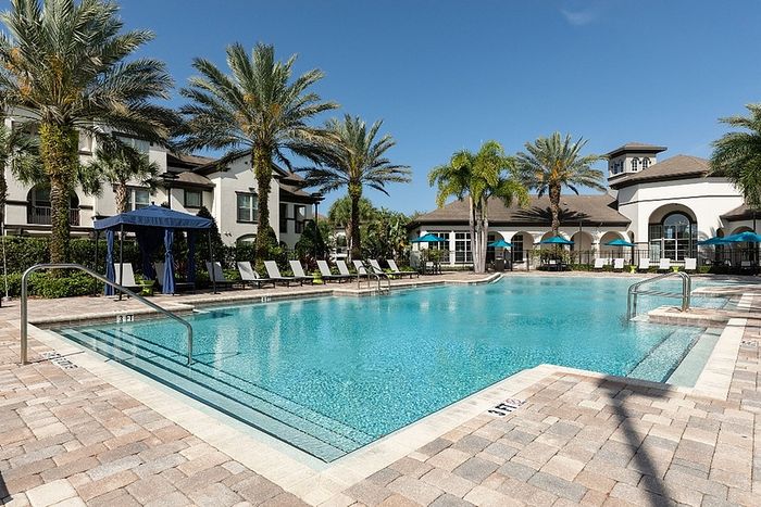 Luxurious apartment complex featuring a stunning swimming pool with palm trees and comfortable sun loungers, perfect for relaxation.