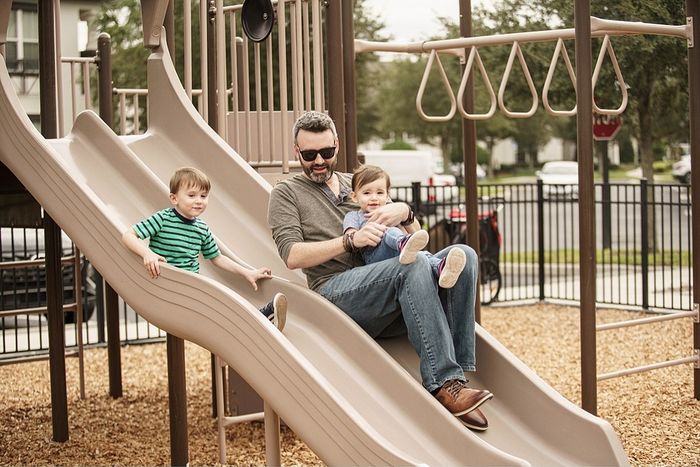 Joyful moment on a playground slide with a father and two smiling children, enjoying a fun day outdoors.
