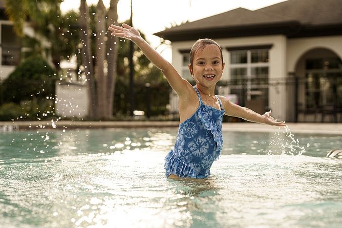 Joyful child playing in a sunlit pool, surrounded by lush greenery and elegant architecture.