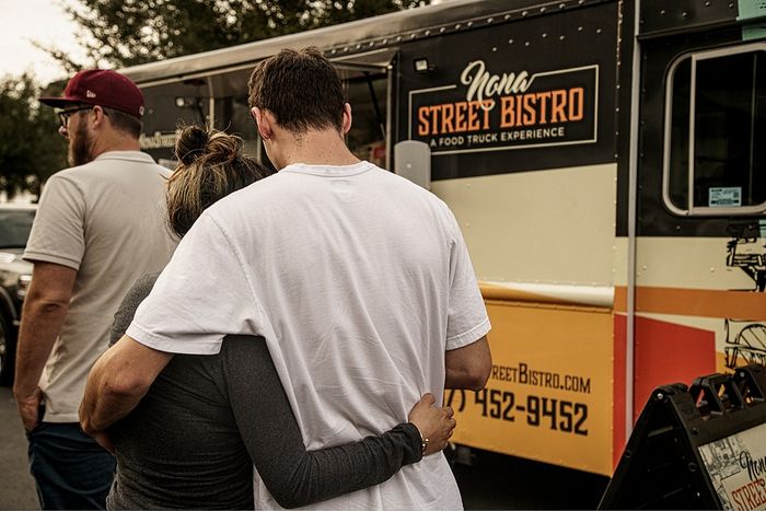 Couple embracing in front of a vibrant food truck with a welcoming street bistro sign, capturing a warm community vibe.
