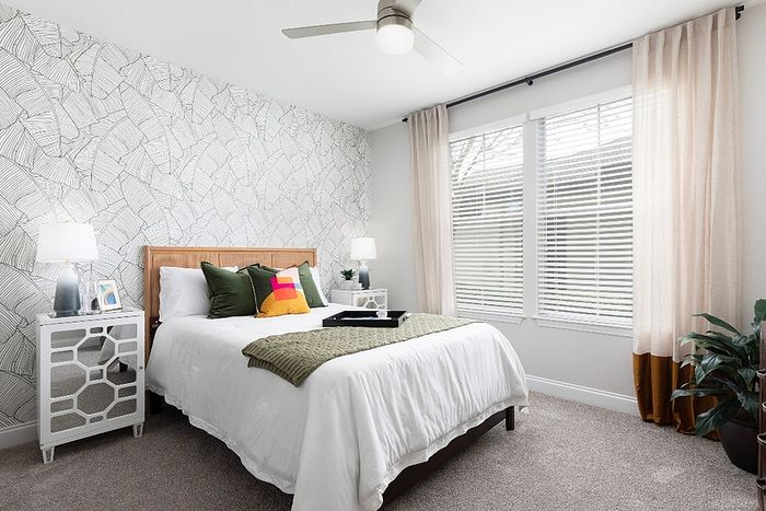 Bright and modern bedroom featuring stylish wallpaper, lush green pillows, and abundant natural light through large windows.