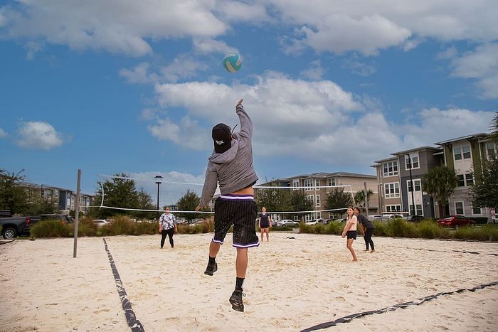 Vibrant community volleyball court with active players surrounded by modern, stylish apartment buildings under a clear blue sky.