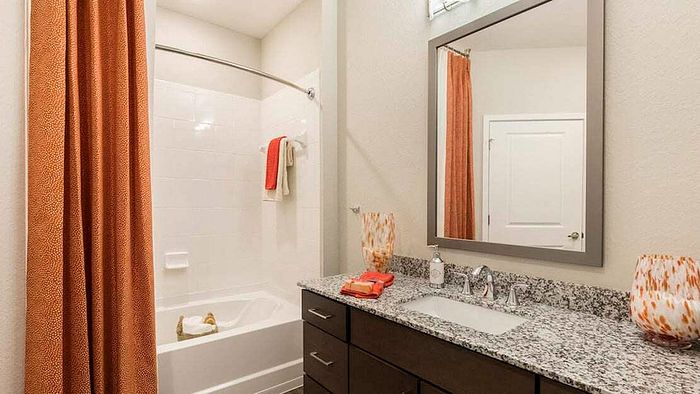 Luxurious bathroom with elegant granite countertop, stylish mirror, and inviting bathtub accented by warm orange hues.