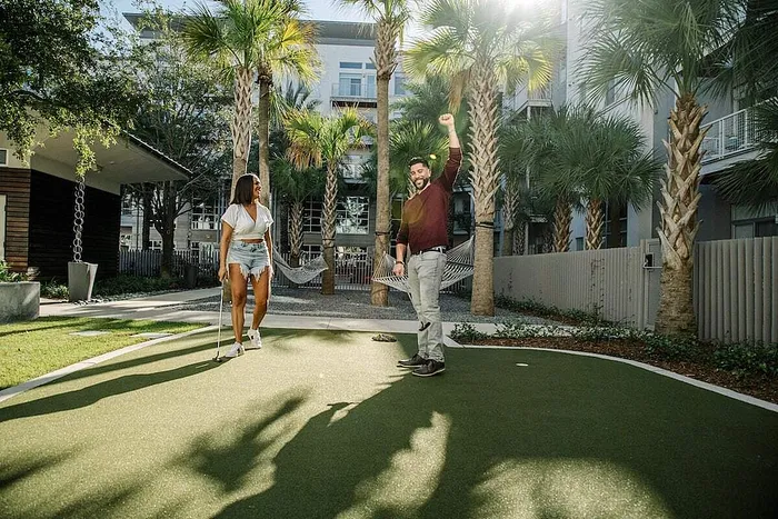 Beautiful outdoor space with palm trees, hammocks, and a mini-golf course, perfect for relaxation and leisure in a modern apartment complex.