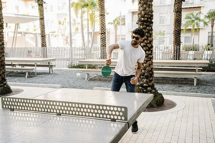 Vibrant outdoor ping pong area in a modern apartment complex with palm trees and relaxed seating.