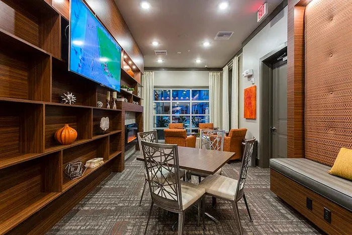 Chic lounge area with elegant wooden shelving, modern decor, cozy seating, and a mounted flat-screen TV under ambient lighting.
