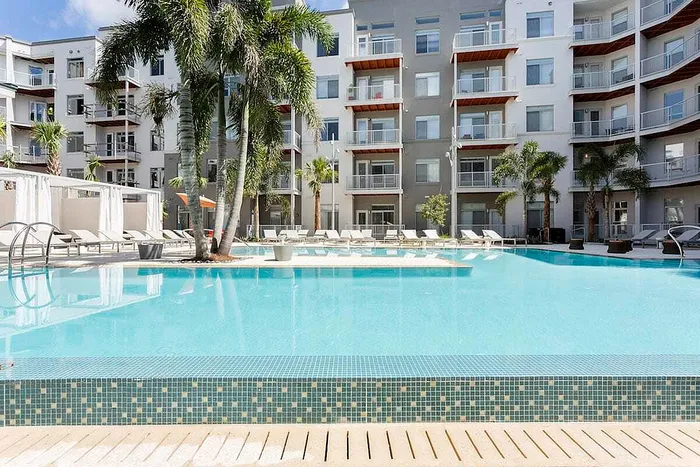 Luxurious apartment complex with a pristine swimming pool, surrounded by modern balconies and tropical palm trees.