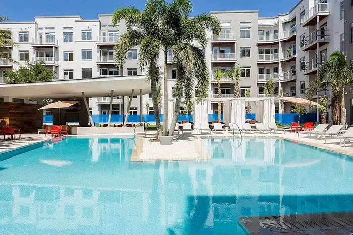 Luxurious apartment complex with a pristine outdoor pool, surrounded by stylish lounge chairs and elegant palm trees for a tropical retreat.