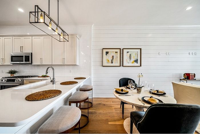 Chic open-plan kitchen and dining area with modern lighting, sleek white cabinetry, and inviting seating.