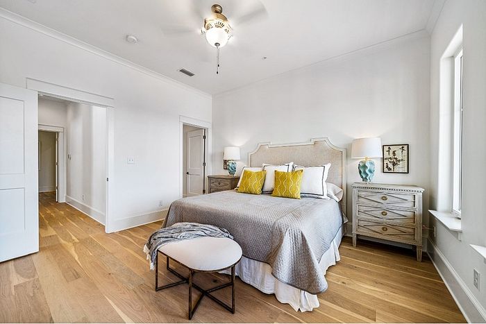 Bright and airy bedroom with elegant d&eacute;cor, highlighting a plush bed with colorful pillows, wooden flooring, and stylish nightstands.