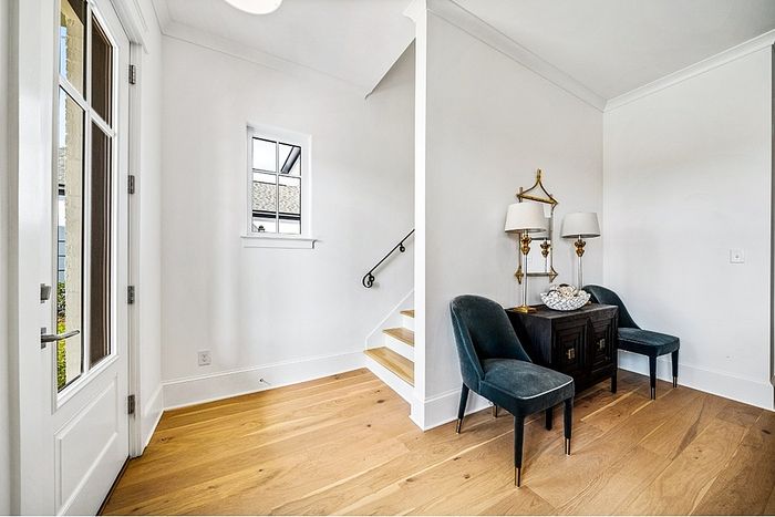 Elegant entryway with rich wood flooring, plush chairs, and charming decor, leading to a staircase with stylish black railing.