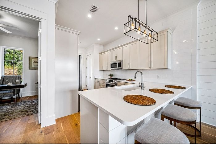 Bright and modern kitchen with sleek white cabinets, elegant countertops, and stylish pendant lighting, featuring an inviting breakfast bar with cozy stools.
