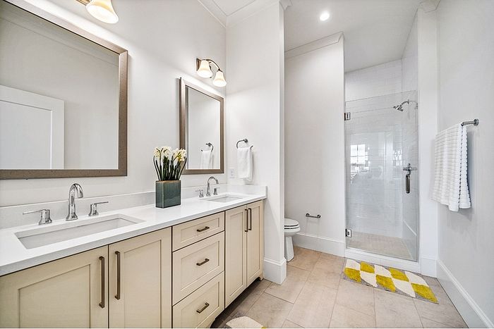 Elegant bathroom with double vanity, stylish mirrors, and a glass-enclosed shower. Cozy and bright with modern lighting.