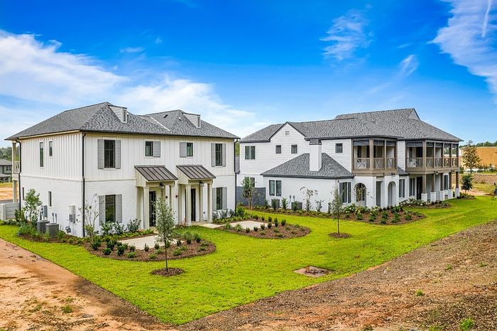 Charming suburban neighborhood with elegant white houses featuring modern architecture, surrounded by lush green lawns and freshly landscaped gardens under a vibrant blue sky.