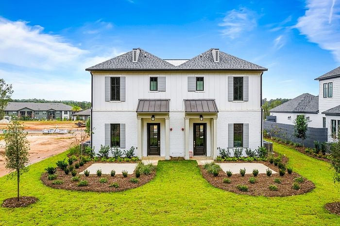 Charming modern duplex with white brick facade, large windows, and beautifully landscaped front yard under a clear blue sky.