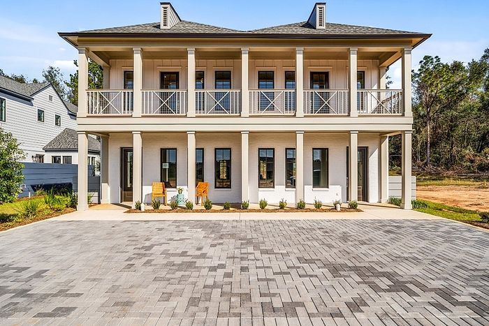 Charming two-story house with classic architecture, spacious front porch, and elegant balcony overlooking a well-maintained driveway.