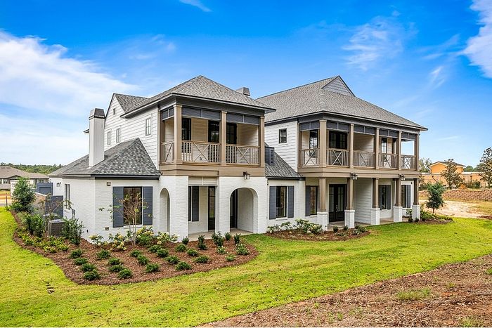 Charming two-story house with elegant balconies, classic architecture, and lush landscaping under a bright blue sky.