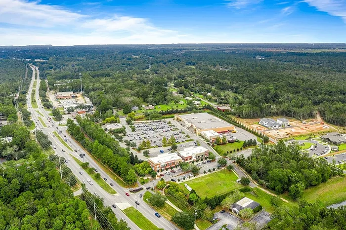 Aerial view showcasing a vibrant mixed-use neighborhood surrounded by lush greenery and expansive landscapes, offering a serene suburban vibe.