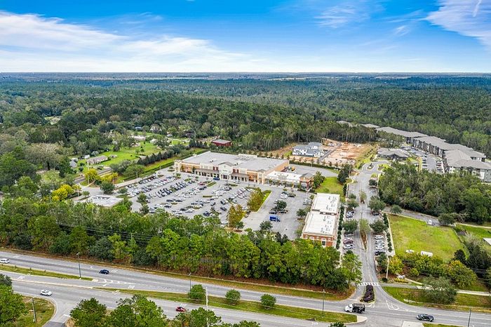 Panoramic aerial view of a vibrant shopping center surrounded by lush greenery and forested landscape, showcasing ample parking and a perfect blend of nature and convenience.