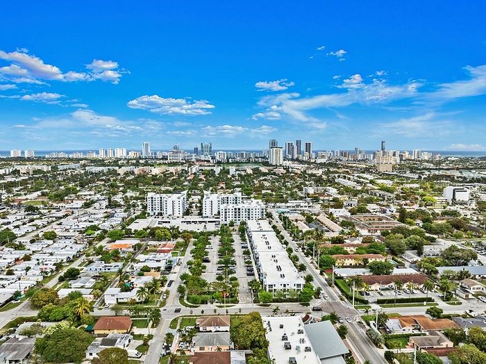 Panoramic aerial view of a vibrant urban landscape with lush greenery, modern buildings, and a clear blue sky.