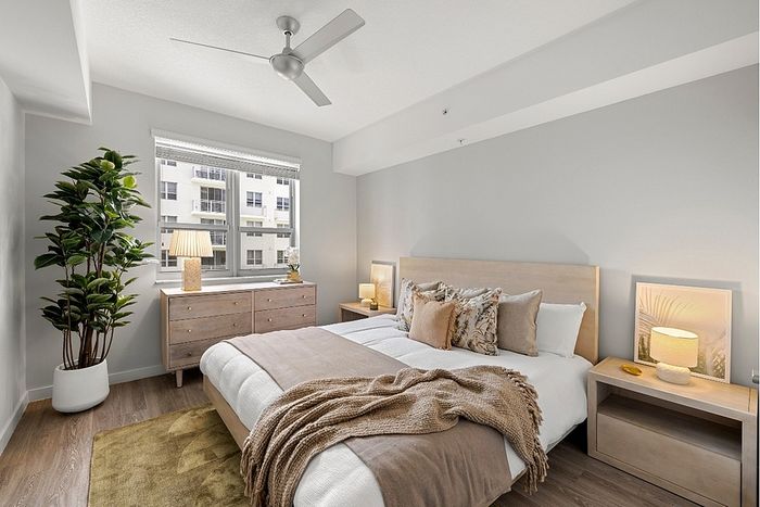 Inviting bedroom with contemporary design, featuring a cozy bed, elegant side tables, green plant, and abundant natural light through a large window.