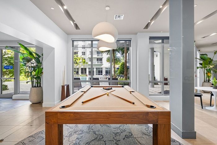 Elegant apartment amenities featuring a chic billiards table in a bright, modern lounge with large windows and lush outdoor views.