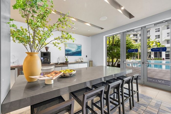 Modern kitchen with sleek countertops and bar seating, vibrant potted plant, and poolside view through glass doors.