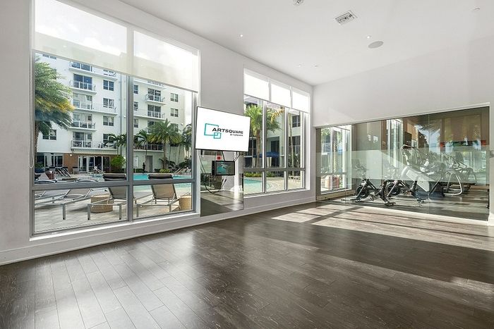 Bright gym space with modern exercise equipment and large windows overlooking a beautiful pool and palm trees.