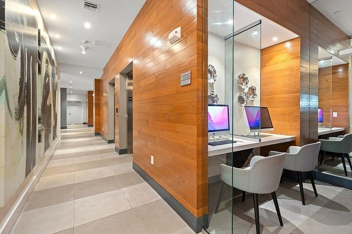 Modern apartment hallway boasting sleek wood paneling and a stylish internet lounge with computers.