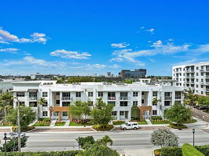 Modern apartment complex with sleek architecture set against a vibrant blue sky, featuring lush landscaping and urban scenery.