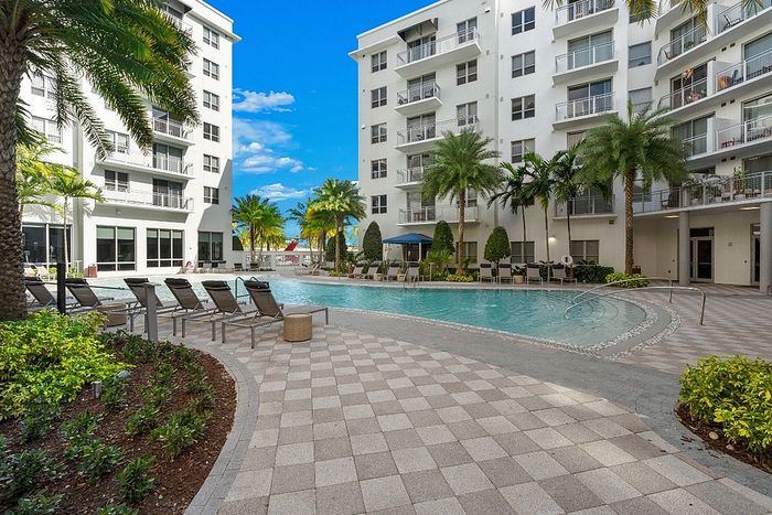 Luxurious apartment complex featuring a pristine swimming pool surrounded by lush palm trees and sun loungers, perfect for relaxation.