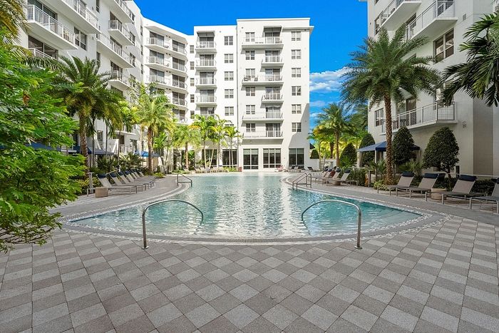Luxurious apartment complex featuring a pristine swimming pool surrounded by tropical palm trees and modern lounge chairs, offering a perfect retreat for relaxation.
