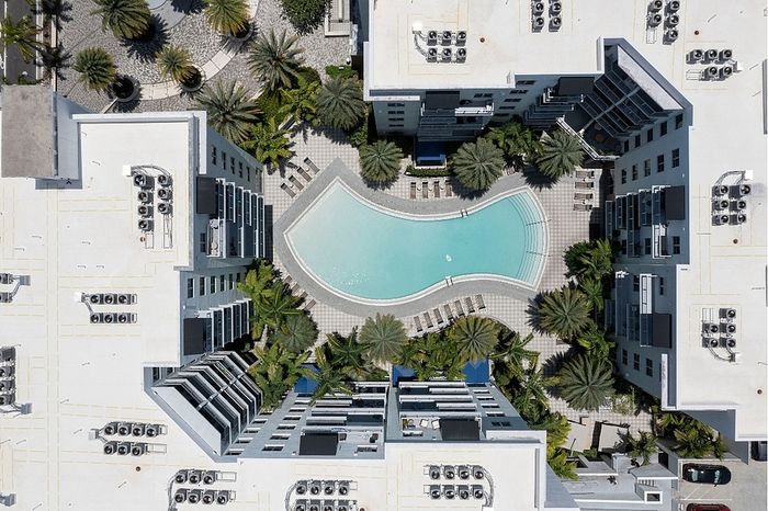 Aerial view of luxury apartment complex with central curved pool, surrounded by palm trees and modern architecture.
