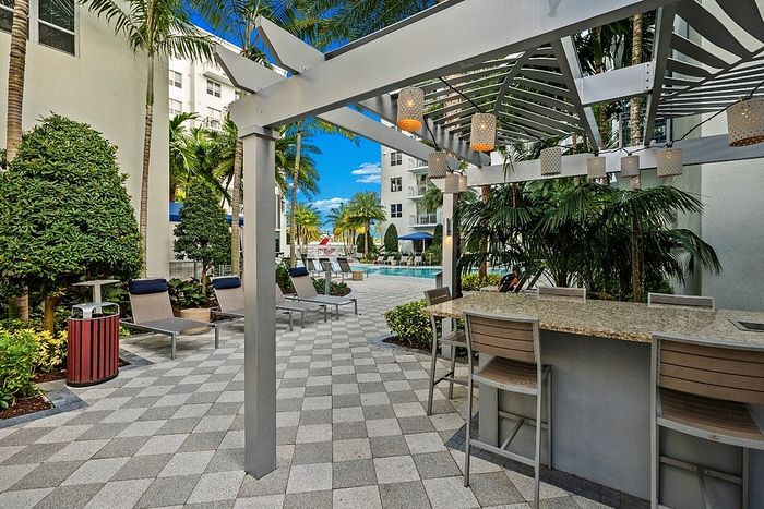 Elegant outdoor patio with stylish pergola, modern seating, and lush greenery leading to a luxurious pool area.