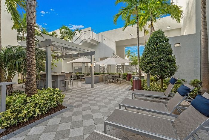 Inviting outdoor lounge area with stylish sun loungers, shaded seating, and lush palm trees under a brilliant blue sky.