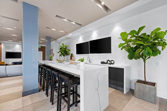 Modern open-concept kitchen with sleek marble countertops, high chairs, elegant decor, and lush green plants.