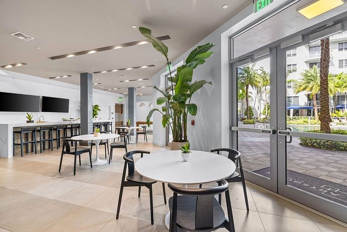 Bright and modern communal area with stylish seating, large indoor plants, and views of a lush exterior, perfect for relaxation and social gatherings.