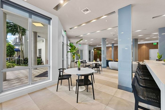 Modern apartment lounge with elegant seating, abundant natural light, and lush green decor, offering a welcoming atmosphere.