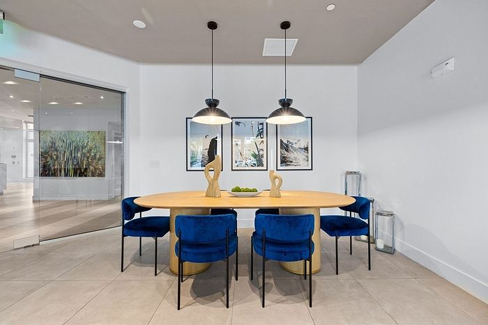 Chic dining area featuring a modern oval wooden table, vibrant blue chairs, and elegant pendant lighting, creating a stylish ambiance.
