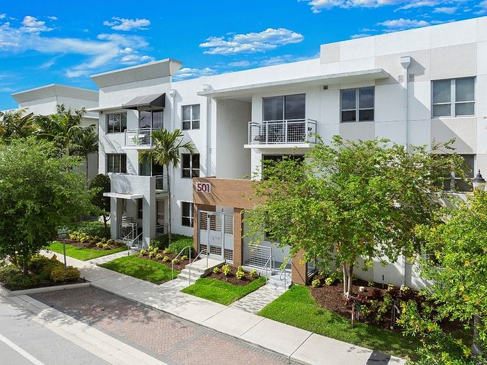 Modern apartment complex featuring stylish white facades, lush landscaping, and private balconies under a vibrant blue sky.