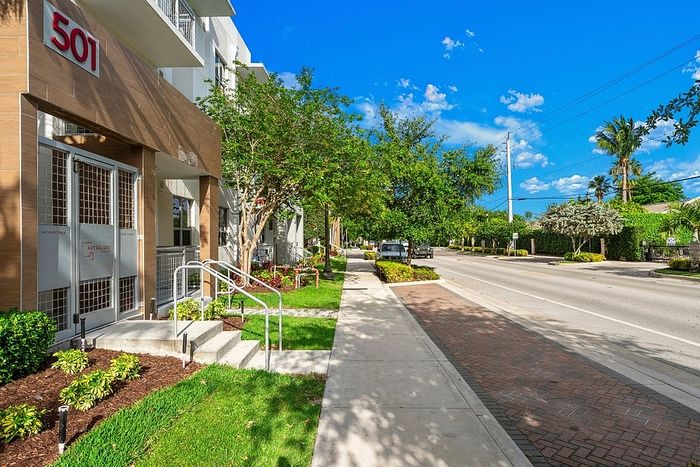 Charming apartment entrance at 501 with lush landscaping and bright blue skies above a quiet sidewalk.