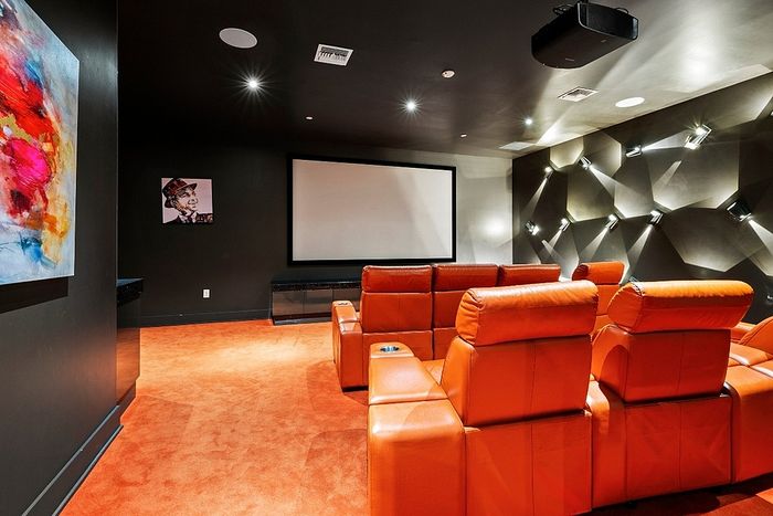 Luxurious home theater with vibrant orange seating, modern art, and advanced soundproofing for the ultimate cinematic experience.