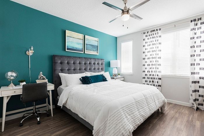Chic bedroom with elegant teal accent wall, cozy white bedding, modern decor, and ample natural light.