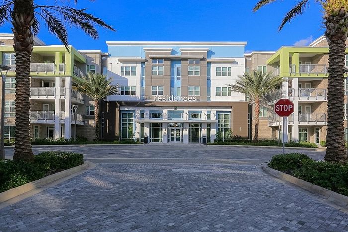 Contemporary apartment complex with lush palm trees and modern architecture under a clear blue sky.