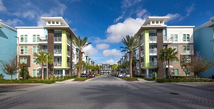 Contemporary apartment complex featuring vibrant facade, lush palm trees, and ample parking under a clear blue sky.