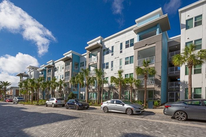 Modern apartment complex with sleek architecture, palm trees, and convenient parking, under a bright blue sky.