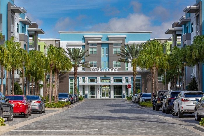 Contemporary apartment complex with sleek architecture, palm-lined entrance, and vibrant surroundings.