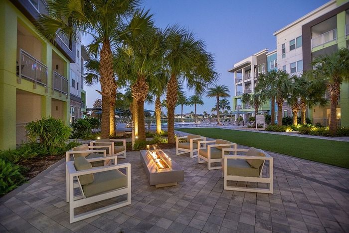 Elegant outdoor seating area with modern fire pit surrounded by palm trees at dusk, in a luxurious apartment community.