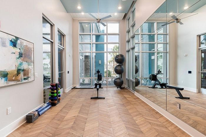 Modern fitness room featuring sleek wood flooring, large windows with abundant natural light, and a selection of exercise equipment for versatile workouts.